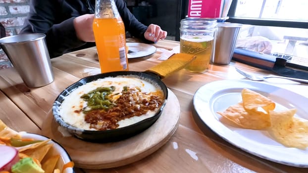 Castle Rock, Colorado, USA-June 12, 2024-Slow motion-Close-up view of a hand picking up a taco from a plate at a restaurant table. The scene features a variety of colorful and appetizing dishes, including nachos topped with cheese and vegetables.