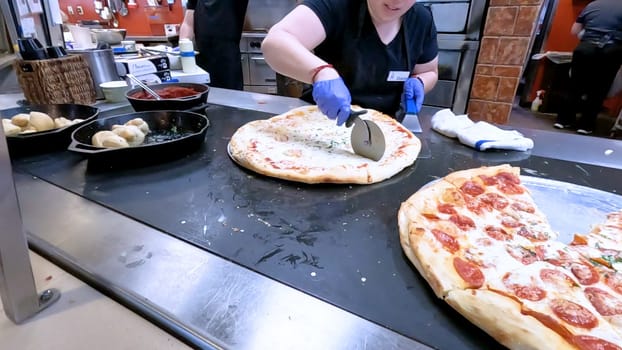 Colorado Springs, Colorado, USA-June 12, 2024-Slow motion-Close-up of a freshly baked pizza slice on a paper plate, placed on a black tray in a pizzeria. The background shows more pizzas being prepared, creating a warm and inviting atmosphere.