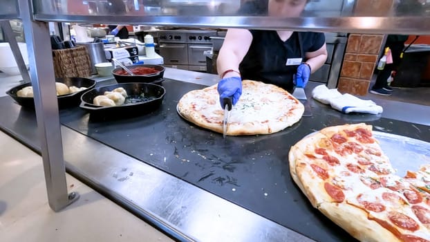 Colorado Springs, Colorado, USA-June 12, 2024-Slow motion-Close-up of a freshly baked pizza slice on a paper plate, placed on a black tray in a pizzeria. The background shows more pizzas being prepared, creating a warm and inviting atmosphere.