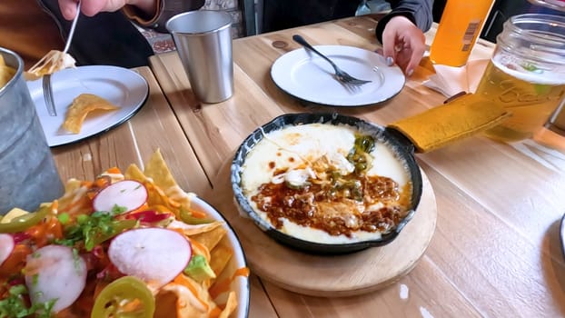 Castle Rock, Colorado, USA-June 12, 2024-Slow motion-Close-up view of a hand picking up a taco from a plate at a restaurant table. The scene features a variety of colorful and appetizing dishes, including nachos topped with cheese and vegetables.