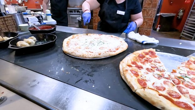 Colorado Springs, Colorado, USA-June 12, 2024-Slow motion-Close-up of a freshly baked pizza slice on a paper plate, placed on a black tray in a pizzeria. The background shows more pizzas being prepared, creating a warm and inviting atmosphere.