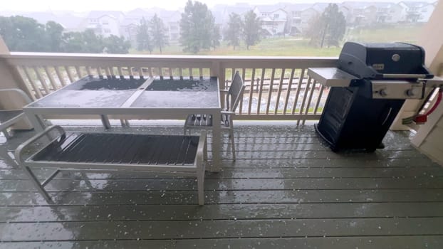 Castle Rock, Colorado, USA-June 12, 2024-Slow motion-Image capturing a hail storm on a wooden deck, highlighting the impact of hail on patio furniture and the deck surface. Hailstones are visible scattered across the wet deck, with patio furniture in the background.