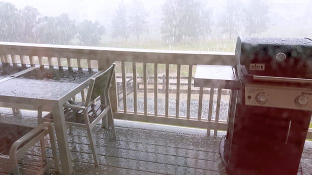 Castle Rock, Colorado, USA-June 12, 2024-Slow motion-Image capturing a hail storm on a wooden deck, highlighting the impact of hail on patio furniture and the deck surface. Hailstones are visible scattered across the wet deck, with patio furniture in the background.