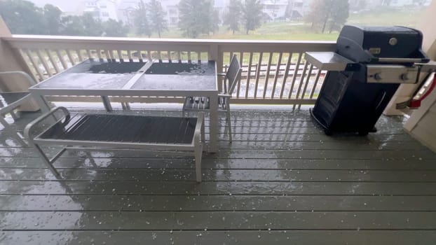 Castle Rock, Colorado, USA-June 12, 2024-Slow motion-Image capturing a hail storm on a wooden deck, highlighting the impact of hail on patio furniture and the deck surface. Hailstones are visible scattered across the wet deck, with patio furniture in the background.