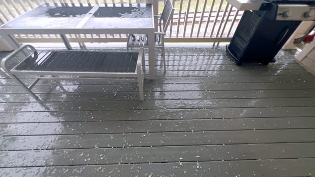 Castle Rock, Colorado, USA-June 12, 2024-Slow motion-Image capturing a hail storm on a wooden deck, highlighting the impact of hail on patio furniture and the deck surface. Hailstones are visible scattered across the wet deck, with patio furniture in the background.