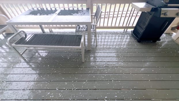 Castle Rock, Colorado, USA-June 12, 2024-Slow motion-Image capturing a hail storm on a wooden deck, highlighting the impact of hail on patio furniture and the deck surface. Hailstones are visible scattered across the wet deck, with patio furniture in the background.