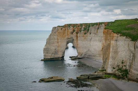 Landscape photo of tall, steep limestone cliffs by the ocean with one with a hole in it creating an arch