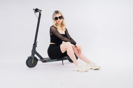 A blonde woman on a red background sitting on electro scooter and resting, copy space