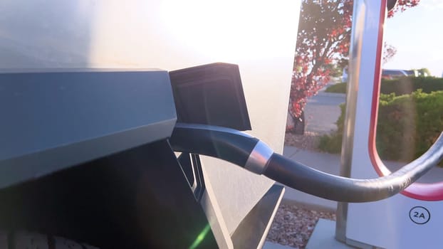 Santa Fe, New Mexico, USA-June 10, 2024-Slow motion-A Tesla Cybertruck is connected to a Tesla Supercharger at an outdoor charging station. The sleek, angular design of the Cybertruck is highlighted by the sunlight, emphasizing its modern and futuristic appearance.