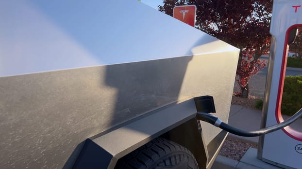 Santa Fe, New Mexico, USA-June 10, 2024-Slow motion-A Tesla Cybertruck is connected to a Tesla Supercharger at an outdoor charging station. The sleek, angular design of the Cybertruck is highlighted by the sunlight, emphasizing its modern and futuristic appearance.