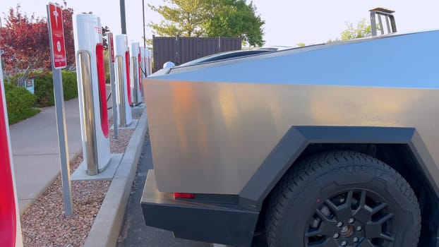 Santa Fe, New Mexico, USA-June 10, 2024-Slow motion-A Tesla Cybertruck is connected to a Tesla Supercharger at an outdoor charging station. The sleek, angular design of the Cybertruck is highlighted by the sunlight, emphasizing its modern and futuristic appearance.