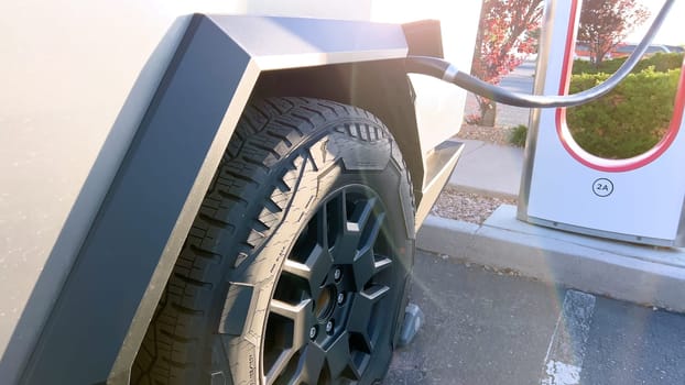 Santa Fe, New Mexico, USA-June 10, 2024-Slow motion-A Tesla Cybertruck is connected to a Tesla Supercharger at an outdoor charging station. The sleek, angular design of the Cybertruck is highlighted by the sunlight, emphasizing its modern and futuristic appearance.