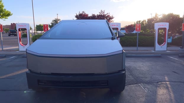 Santa Fe, New Mexico, USA-June 10, 2024-Slow motion-A Tesla Cybertruck is connected to a Tesla Supercharger at an outdoor charging station. The sleek, angular design of the Cybertruck is highlighted by the sunlight, emphasizing its modern and futuristic appearance.