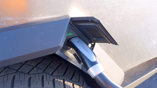 Santa Fe, New Mexico, USA-June 10, 2024-Slow motion-A Tesla Cybertruck is connected to a Tesla Supercharger at an outdoor charging station. The sleek, angular design of the Cybertruck is highlighted by the sunlight, emphasizing its modern and futuristic appearance.