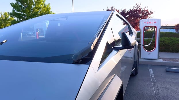 Santa Fe, New Mexico, USA-June 10, 2024-Slow motion-A Tesla Cybertruck is connected to a Tesla Supercharger at an outdoor charging station. The sleek, angular design of the Cybertruck is highlighted by the sunlight, emphasizing its modern and futuristic appearance.