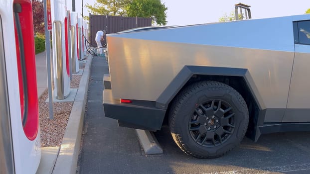 Santa Fe, New Mexico, USA-June 10, 2024-Slow motion-A Tesla Cybertruck is connected to a Tesla Supercharger at an outdoor charging station. The sleek, angular design of the Cybertruck is highlighted by the sunlight, emphasizing its modern and futuristic appearance.