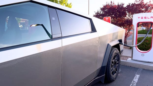 Santa Fe, New Mexico, USA-June 10, 2024-Slow motion-A Tesla Cybertruck is connected to a Tesla Supercharger at an outdoor charging station. The sleek, angular design of the Cybertruck is highlighted by the sunlight, emphasizing its modern and futuristic appearance.