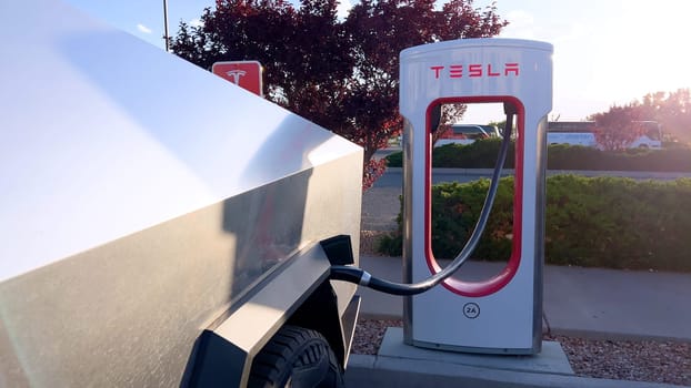 Santa Fe, New Mexico, USA-June 10, 2024-Slow motion-A Tesla Cybertruck is connected to a Tesla Supercharger at an outdoor charging station. The sleek, angular design of the Cybertruck is highlighted by the sunlight, emphasizing its modern and futuristic appearance.