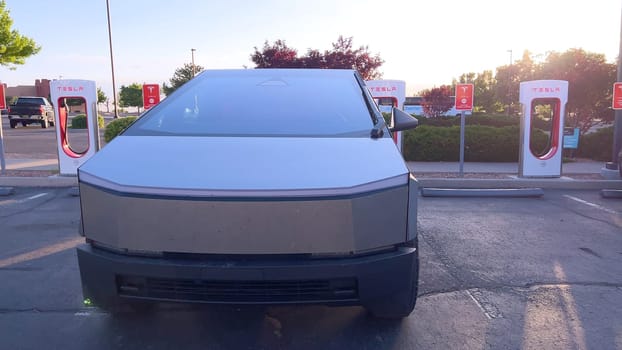 Santa Fe, New Mexico, USA-June 10, 2024-Slow motion-A Tesla Cybertruck is connected to a Tesla Supercharger at an outdoor charging station. The sleek, angular design of the Cybertruck is highlighted by the sunlight, emphasizing its modern and futuristic appearance.