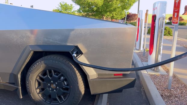 Santa Fe, New Mexico, USA-June 10, 2024-Slow motion-A Tesla Cybertruck is connected to a Tesla Supercharger at an outdoor charging station. The sleek, angular design of the Cybertruck is highlighted by the sunlight, emphasizing its modern and futuristic appearance.