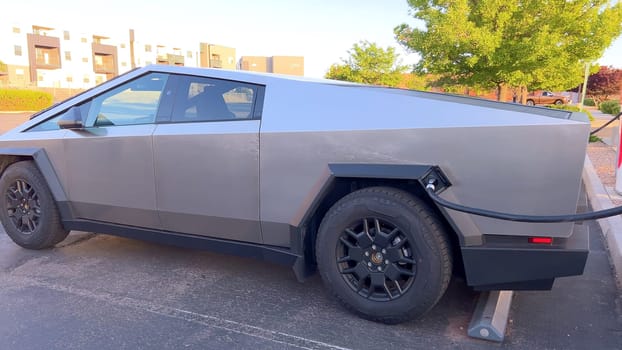 Santa Fe, New Mexico, USA-June 10, 2024-Slow motion-A Tesla Cybertruck is connected to a Tesla Supercharger at an outdoor charging station. The sleek, angular design of the Cybertruck is highlighted by the sunlight, emphasizing its modern and futuristic appearance.