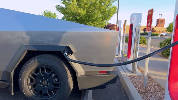 Santa Fe, New Mexico, USA-June 10, 2024-Slow motion-A Tesla Cybertruck is connected to a Tesla Supercharger at an outdoor charging station. The sleek, angular design of the Cybertruck is highlighted by the sunlight, emphasizing its modern and futuristic appearance.