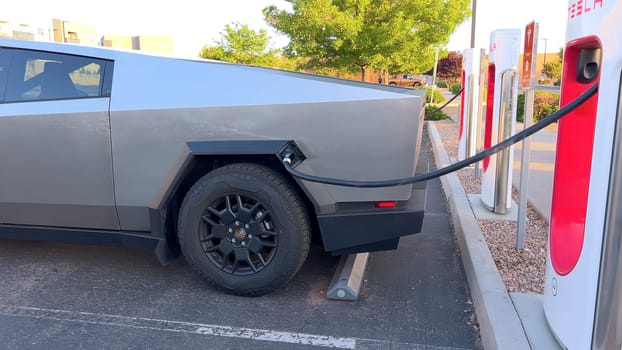 Santa Fe, New Mexico, USA-June 10, 2024-Slow motion-A Tesla Cybertruck is connected to a Tesla Supercharger at an outdoor charging station. The sleek, angular design of the Cybertruck is highlighted by the sunlight, emphasizing its modern and futuristic appearance.