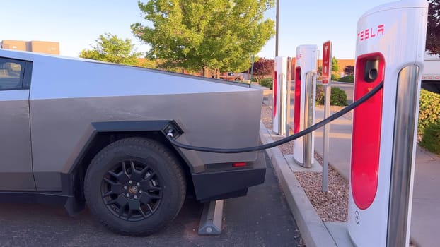 Santa Fe, New Mexico, USA-June 10, 2024-Slow motion-A Tesla Cybertruck is connected to a Tesla Supercharger at an outdoor charging station. The sleek, angular design of the Cybertruck is highlighted by the sunlight, emphasizing its modern and futuristic appearance.