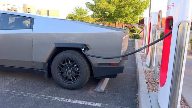 Santa Fe, New Mexico, USA-June 10, 2024-Slow motion-A Tesla Cybertruck is connected to a Tesla Supercharger at an outdoor charging station. The sleek, angular design of the Cybertruck is highlighted by the sunlight, emphasizing its modern and futuristic appearance.