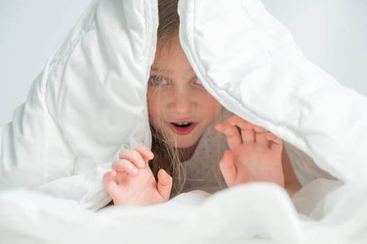 Portrait of a cute little girl laughing and hiding under the blanket