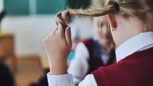 A girl touches a braid of her hair during class