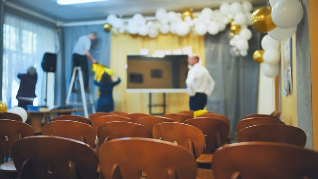 Teachers prepare the hall for a school event. Focus focus on the chairs.