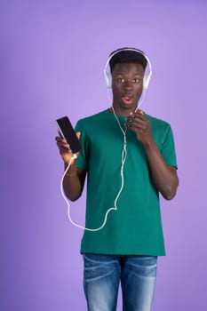 A man wearing headphones is holding a cell phone in his hand, appearing to be engaged with the device.