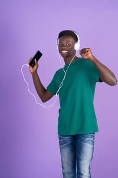 A man wearing headphones is holding a remote control while engaging with electronic devices.