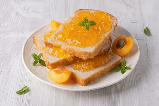Toasts with tasty apricot jam on a white wooden table.