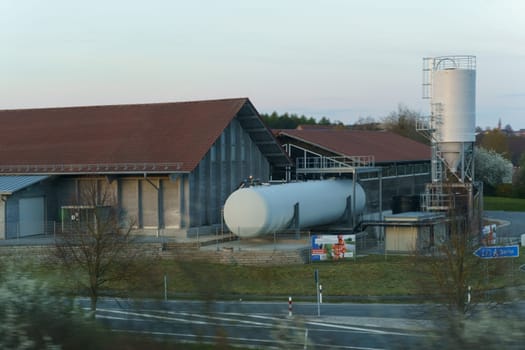 Bayreuth, Germany - April 30, 2023: A factory stands tall in the background with a massive tank in the front, representing industrial infrastructure and storage facilities.