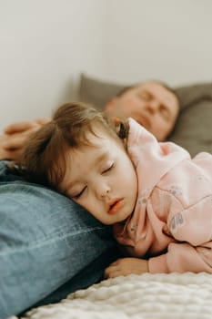 Portrait of a beautiful and cute sleeping girl on the legs of her sleeping father lying on the sofa during the day in the living room, close-up side view with depth of field. Family vacation concept, healthy sleep, dads.