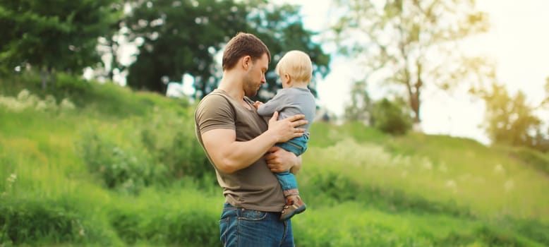 Young caucasian father holding his son, dad and child walking together in summer park