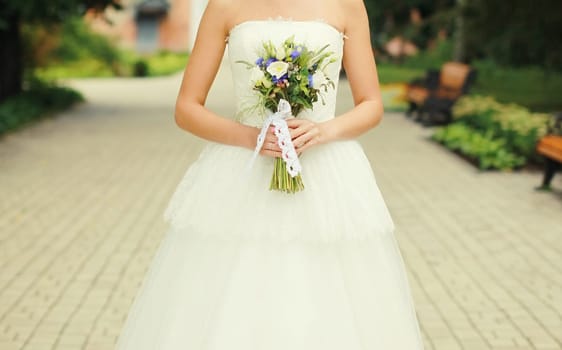 Beautiful lovely bride in white wedding dress holding bouquet of flowers outdoors