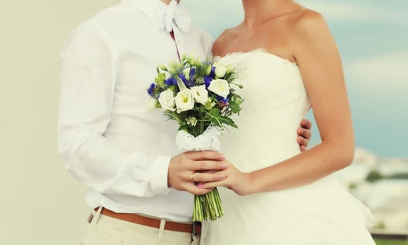 Wedding couple, bride in white dress with bouquet of flowers and groom in shirt holding hands outdoors
