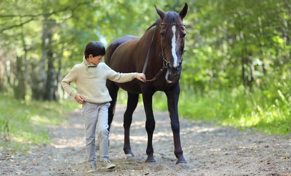 Teenager boy kid standing with horse walking in summer forest, horseback riding