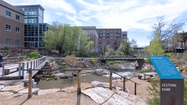 Castle Rock, Colorado, USA-June 12, 2024-Slow motion-A picturesque view of Downtown Castle Rock, Colorado, featuring a serene river flowing through the urban landscape. The scene includes a charming bridge, lush greenery, and modern buildings in the background under a bright blue sky with scattered clouds. The blend of nature and urban development highlights the unique character of this vibrant community.