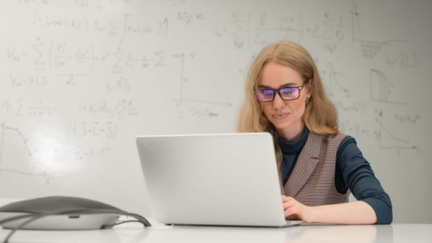 Caucasian woman scientist typing on laptop. White board with formulas