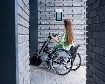 A woman in a wheelchair with an assistive device for manual control enters the entrance. Electric hand bike