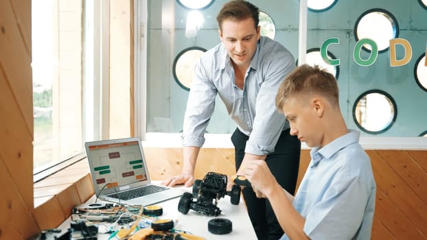 Caucasian teacher help student fixing car model and giving advise for programing system or coding prompt while highschool boy listen and use equipment to repair robot at STEM classroom. Edification.