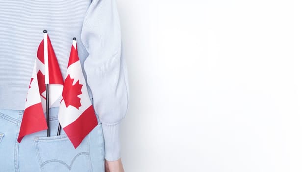 A miniature Canadian flag stands out of the back pocket of blue jeans on an isolated white background. The flag is a symbol of Canada and is often used to show national pride.