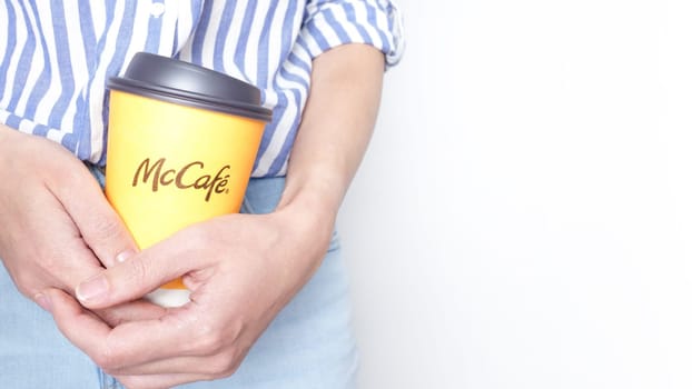 Woman holding a yellow McCafe coffee cup wearing blue jeans and blue striped shirt. Ottawa ON Canada 06-17-2024.