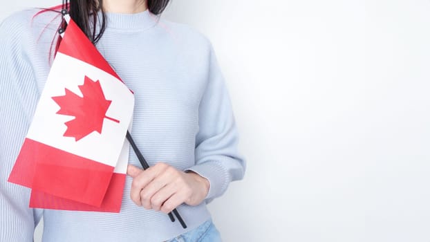 Unrecognized girl student in white blue shirt holding small Canadian flag over gray background, Canada day, holiday, vote, immigration, tax, copy space.