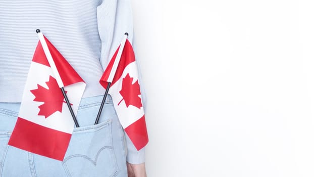 A miniature Canadian flag stands out of the back pocket of blue jeans on an isolated white background. The flag is a symbol of Canada and is often used to show national pride.