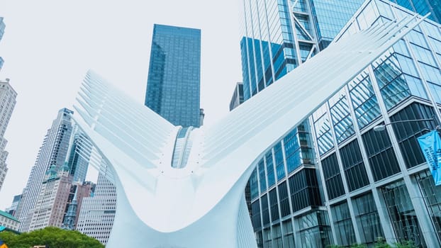 A modern sculpture of large white wings stands in front of a backdrop of skyscrapers in a major city. The sculpture is a popular tourist attraction and is often used as a meeting place.